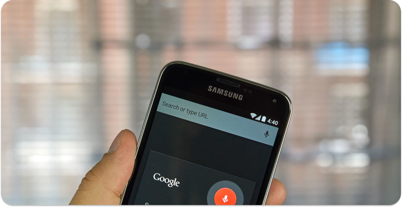 Hand holding a smartphone with Google's voice search ready, symbolizing dictation software.