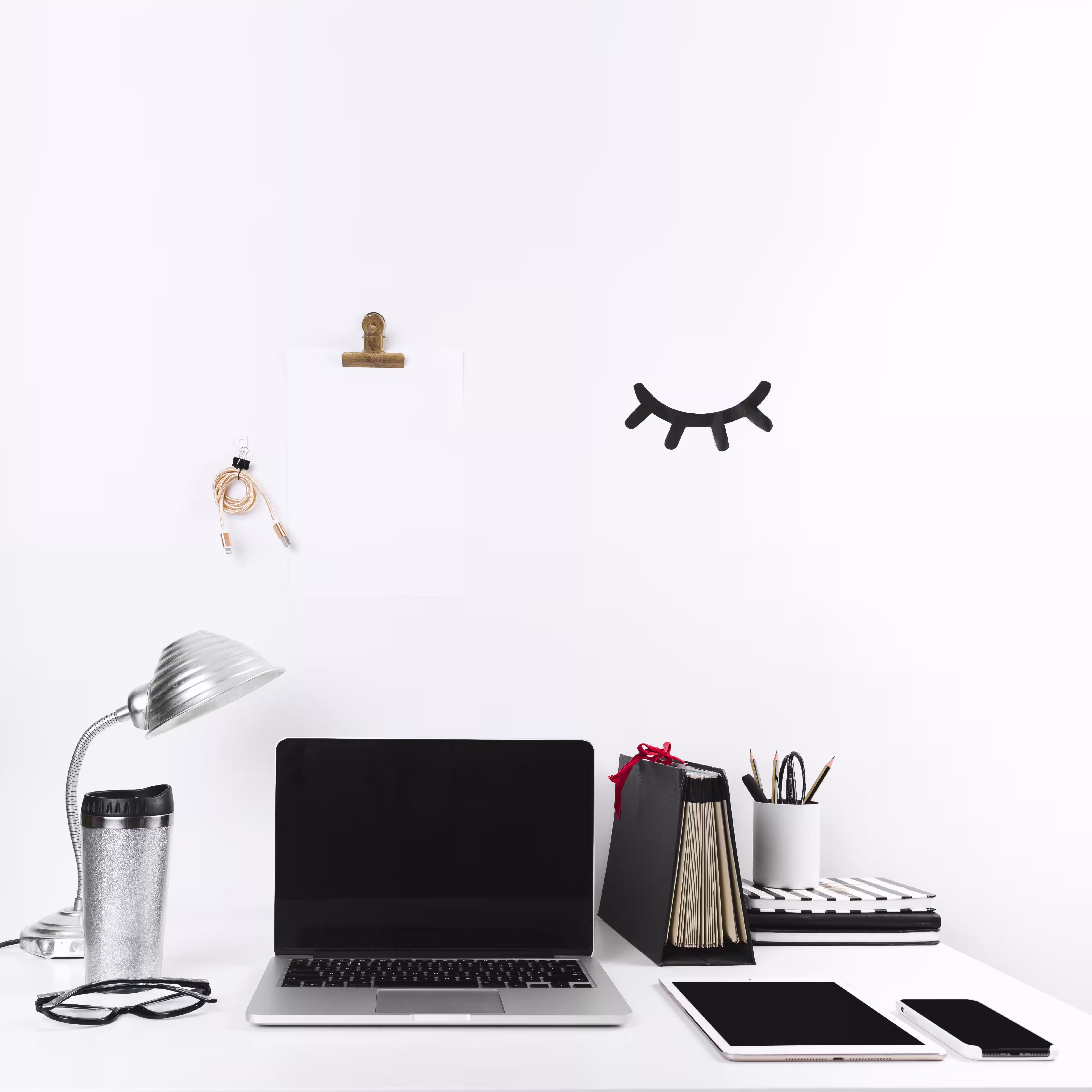 Organized white desk with laptop, tablet, phone, and minimal office supplies against clean wall