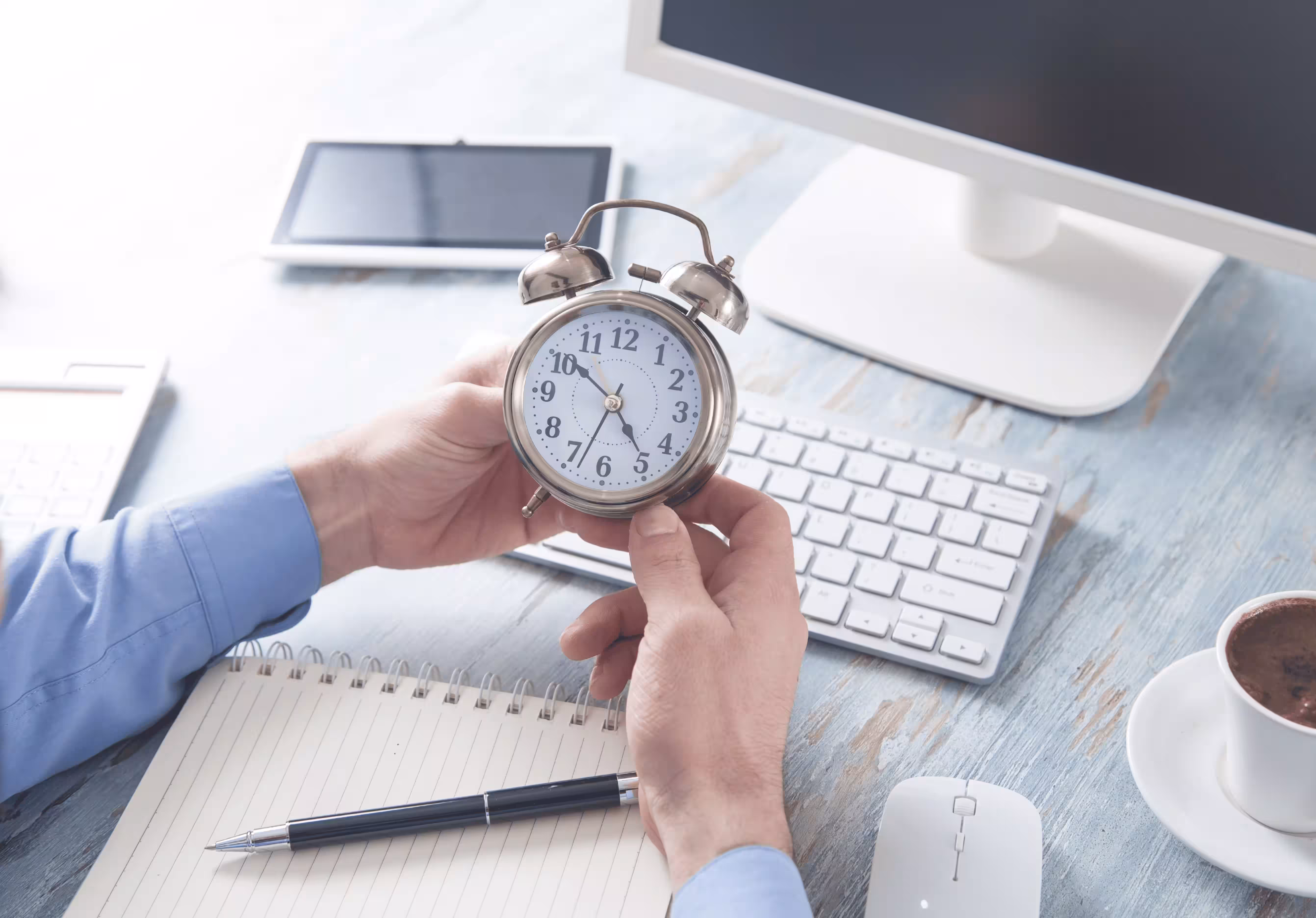 Hand holding vintage alarm clock against desktop computer workspace