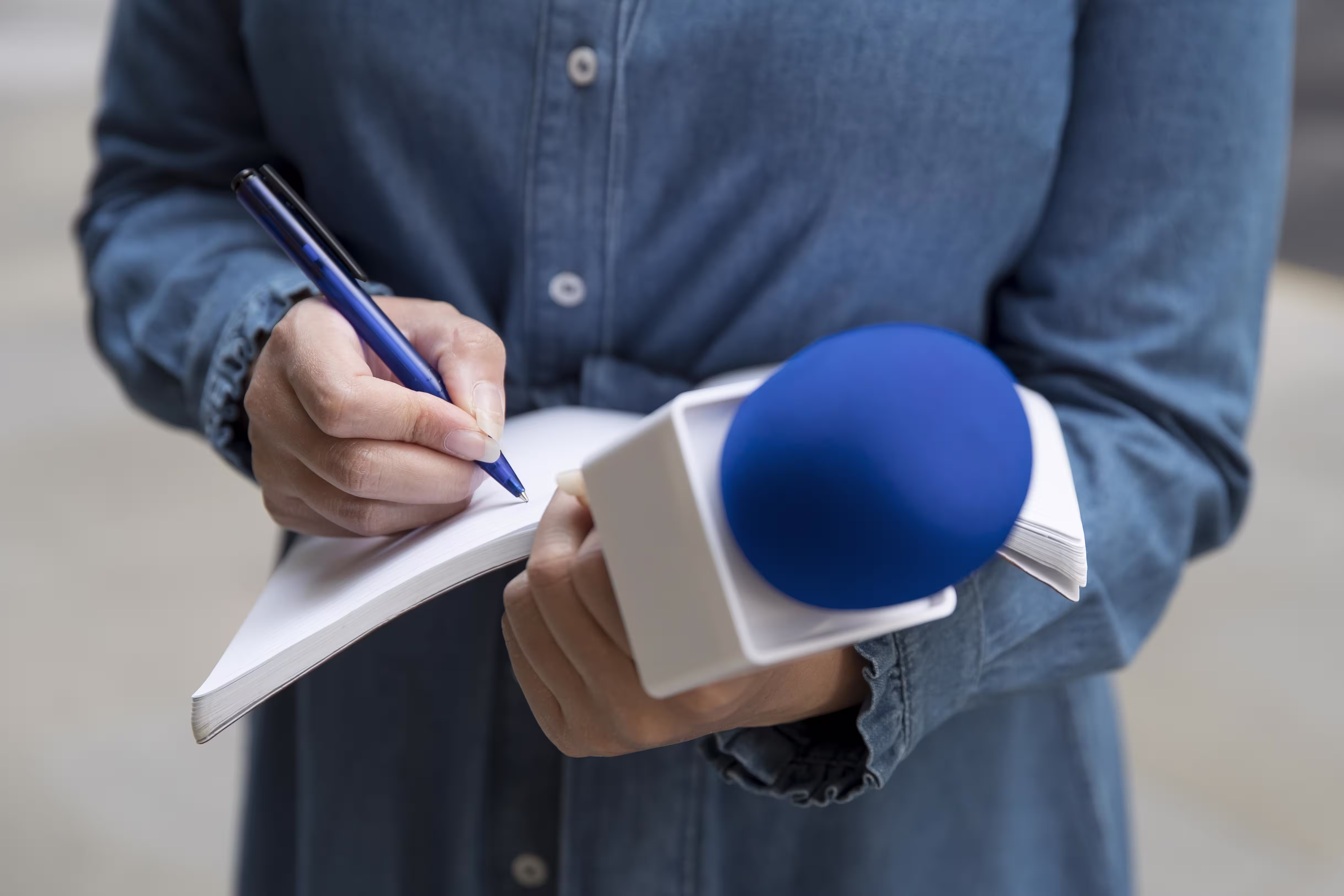 Person holding a notebook and blue microphone while taking notes during an interview.