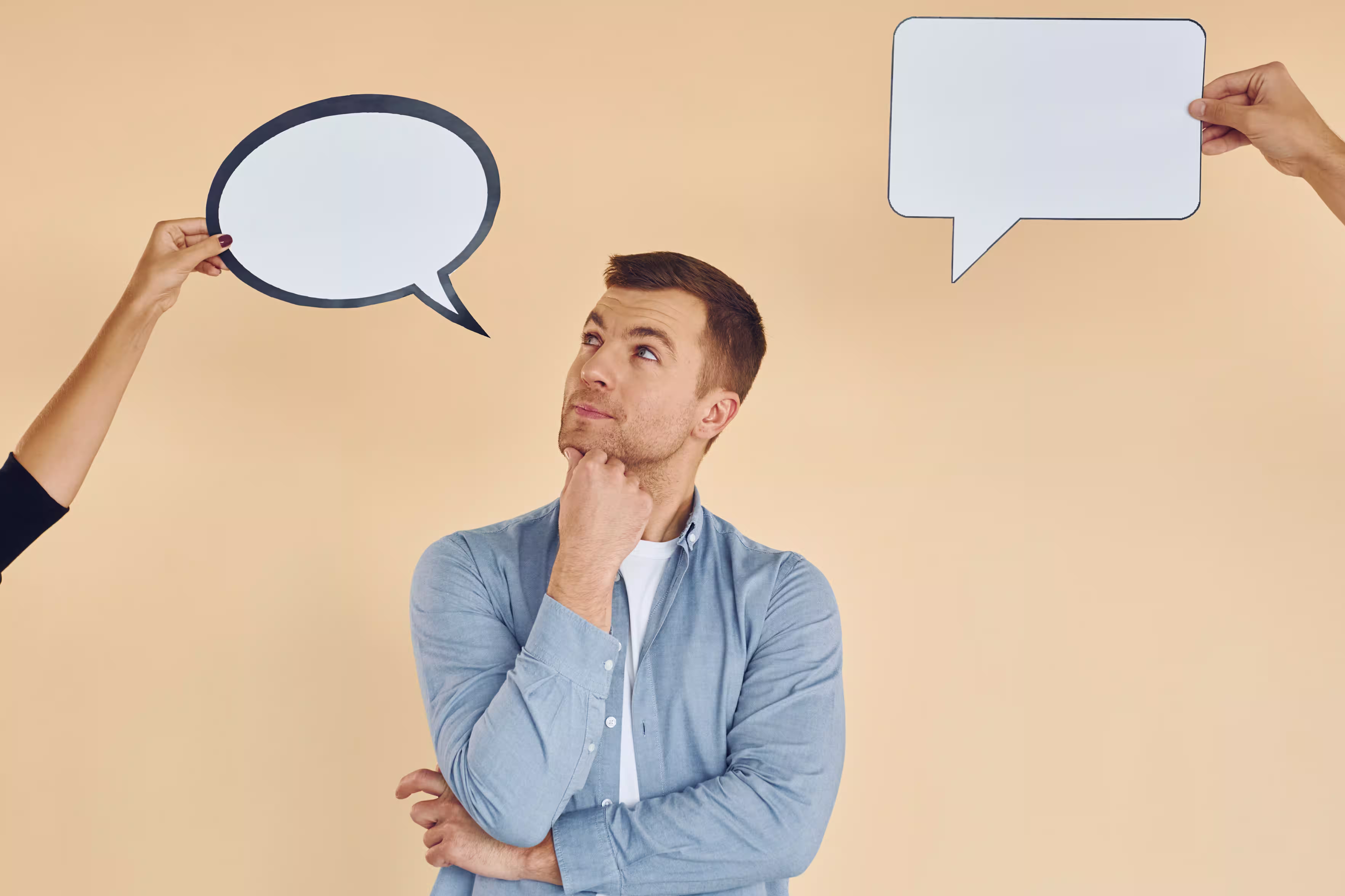 Person with thoughtful expression considering two empty speech bubbles while resting hand on chin