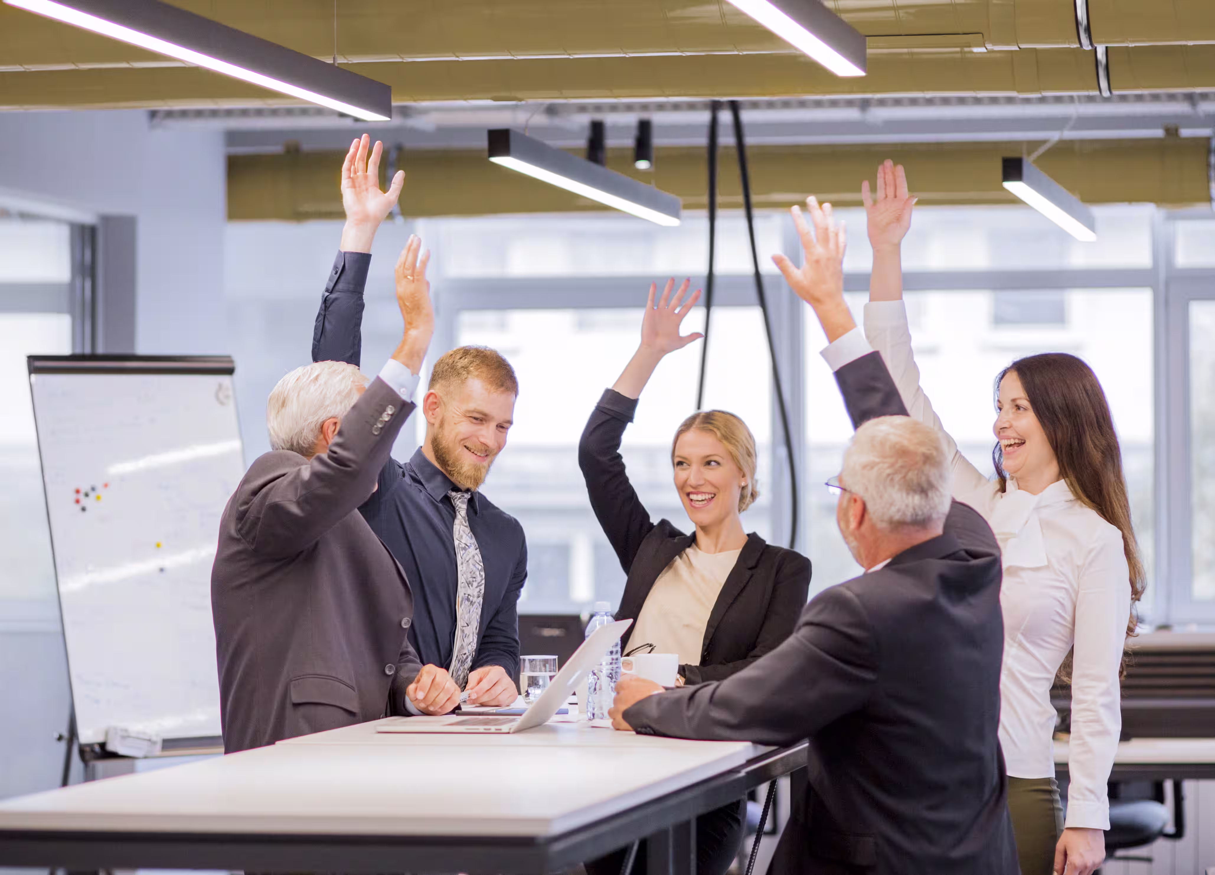 Business professionals raising hands in excitement during a modern office meeting