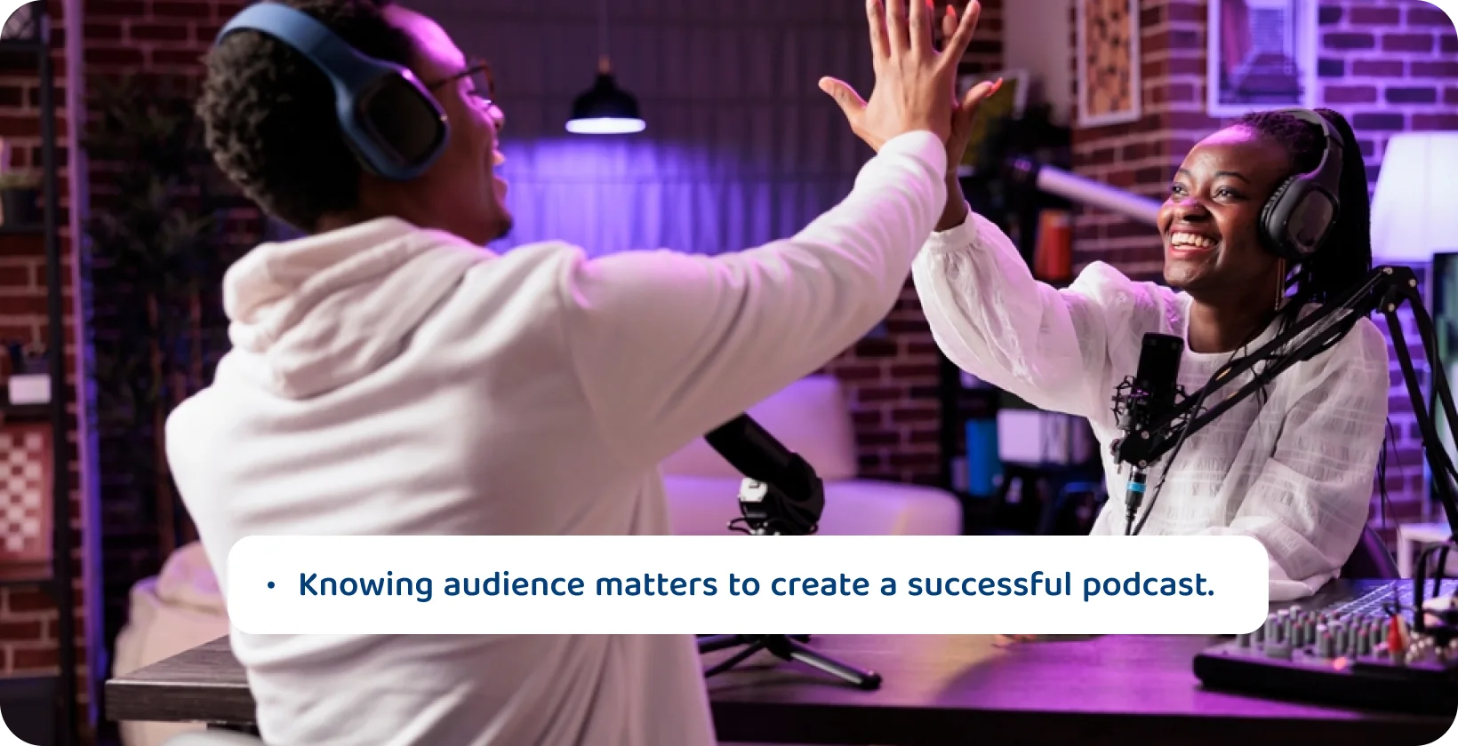 Host podcast melakukan high-fiving dalam pengaturan studio, menandakan kegembiraan mengetahui audiens mereka untuk kesuksesan podcast.