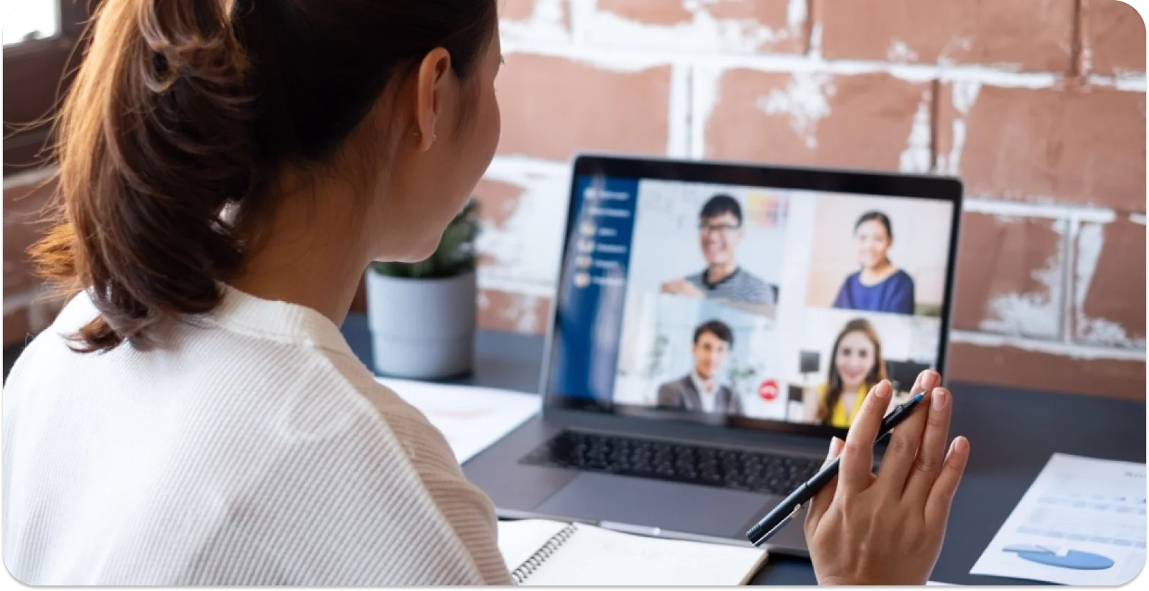 Profesional terlibat dalam rapat virtual dengan kolega di layar laptop.